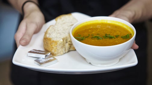 Someone holding a bowl of soup with bread on the side